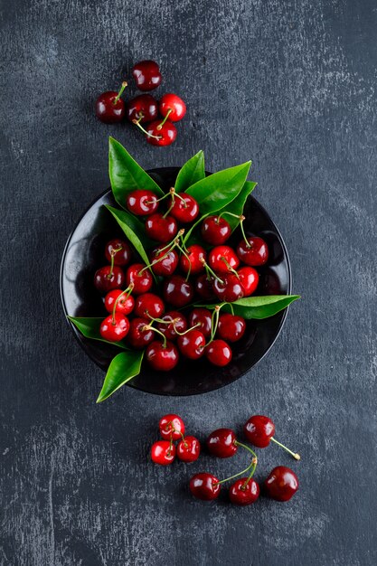 Cerezas con hojas en un plato sobre superficie gris, vista superior