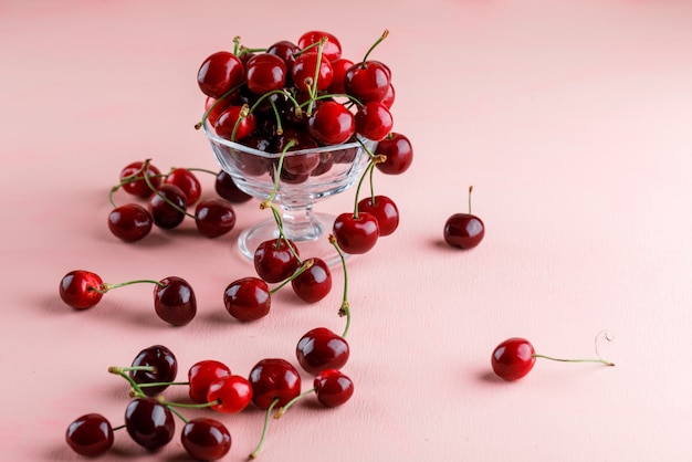 Cerezas en un jarrón sobre una superficie rosa