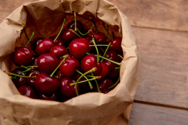 Cerezas en paquete de papel artesanal en mesa de madera