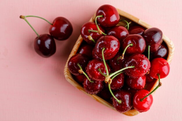 Cerezas en un plato de madera sobre una superficie plana de color rosa.