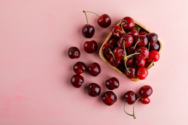 Foto gratuita cerezas en un plato de madera sobre superficie rosa