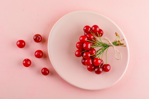 Las cerezas en un plato plano yacían sobre una mesa rosa