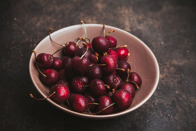 Cerezas en un recipiente en un marrón oscuro. Vista de ángulo alto.