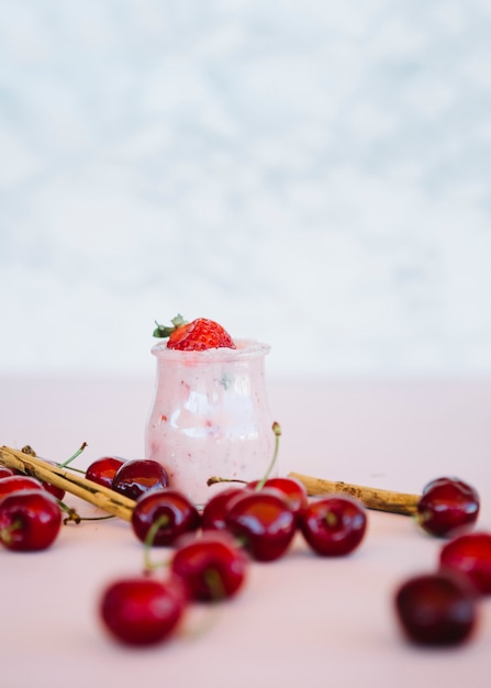 Cerezas rojas con batido de fresa en superficie rosa