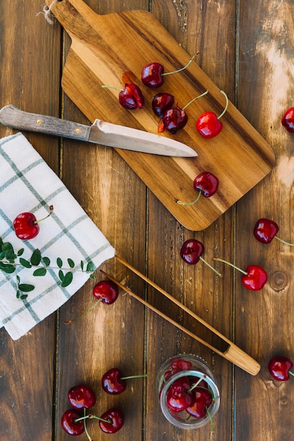 Foto gratuita cerezas rojas frescas y cuchillo en la tabla de cortar de madera