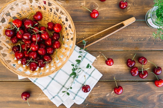 Cerezas rojas frescas en un recipiente de mimbre sobre fondo de madera