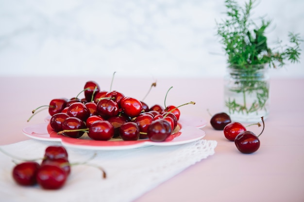 Cerezas rojas jugosas en placa sobre escritorio rosa