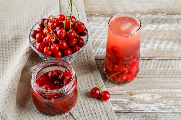 Cerezas en un tazón con mermelada, cóctel vista de ángulo alto en madera y papel de cocina