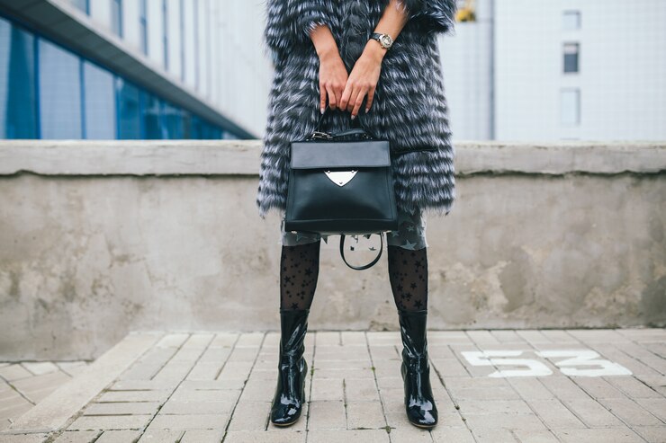Foto gratuito cerrar detalles de accesorios de mujer elegante caminando en la ciudad con abrigo de piel cálido, temporada de invierno, clima frío, sosteniendo el bolso de cuero, piernas con botas, tendencia de moda callejera de calzado