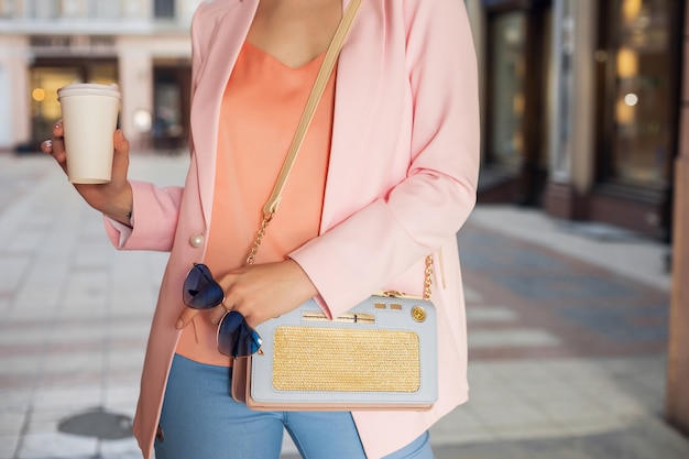 Cerrar detalles de accesorios de mujer en ropa elegante caminando en la calle con gafas de sol, bolso, vestido con chaqueta rosa, tomando café, tendencia de moda primavera verano