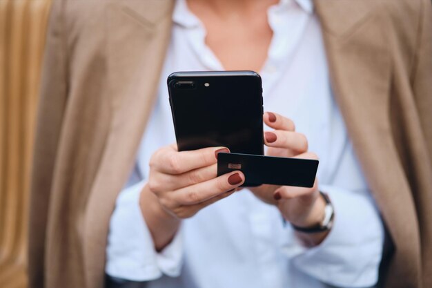 Cerrar elegante mujer de negocios con tarjeta de crédito usando teléfono celular al aire libre