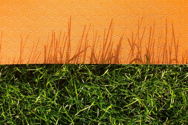 Cerrar estera de yoga naranja sobre hierba verde en el parque al aire libre