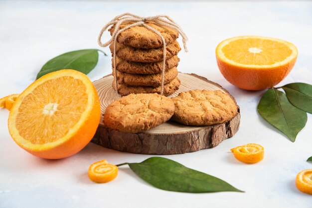 Cerrar foto de galleta casera sobre tabla de madera y media naranja cortada con hojas sobre mesa blanca.