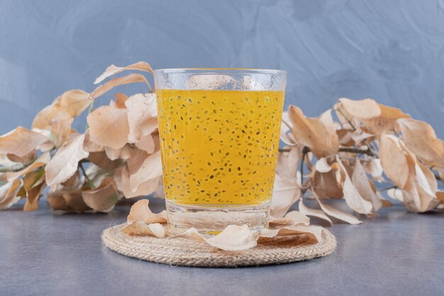 Cerrar foto de jugo de naranja recién hecho con hojas decorativas sobre fondo gris.