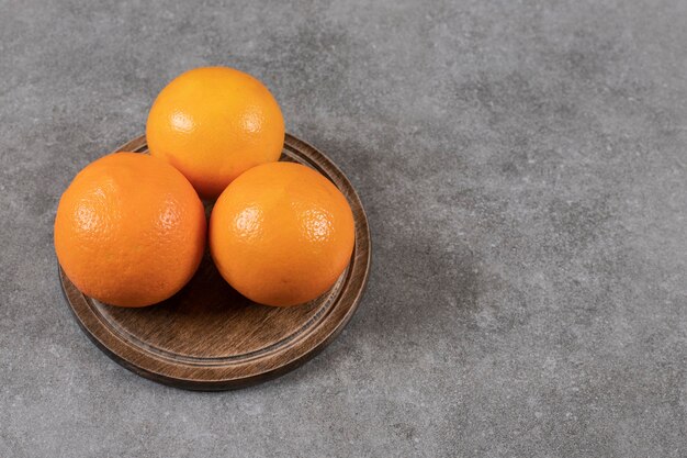 Cerrar foto de naranjas maduras sobre tabla de madera sobre mesa gris.