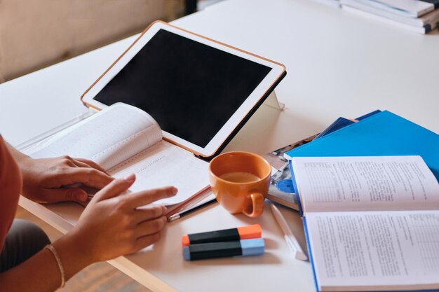 Cerrar foto de niña estudiando con tablettextbooks y taza de café en el escritorio en casa acogedora