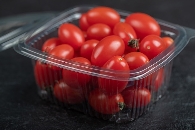 Cerrar foto de pequeños tomates frescos en recipiente de plástico. Foto de alta calidad