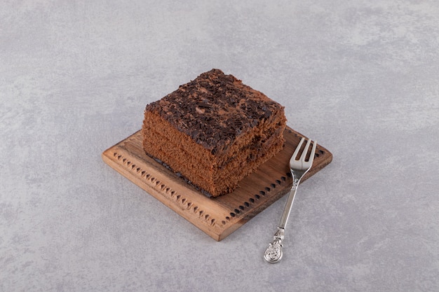 Cerrar foto de rebanada de pastel de chocolate sobre tabla de madera sobre fondo gris.