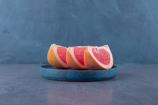 Cerrar foto de rodajas de pomelo orgánico en placa de madera azul.