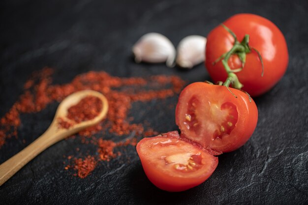 Cerrar foto de tomates maduros enteros o medio cortados con ajo y pimiento rojo sobre fondo negro.