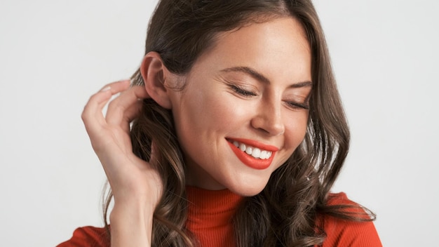 Foto gratuita cerrar hermosa chica morena sonriente posando con encanto en la cámara sobre fondo blanco.