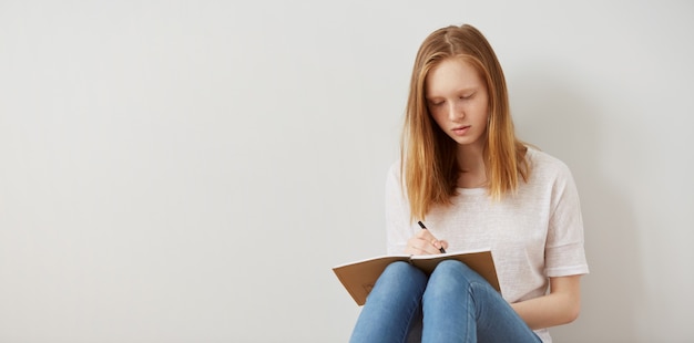 Cerrar imagen de estilo de vida de bastante joven adolescente sentada en su suelo y tomando notas