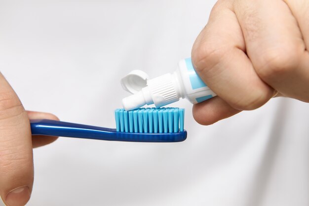 Cerrar imagen de las manos del hombre sosteniendo el tubo, apretando la pasta de dientes blanqueadora en el cepillo.