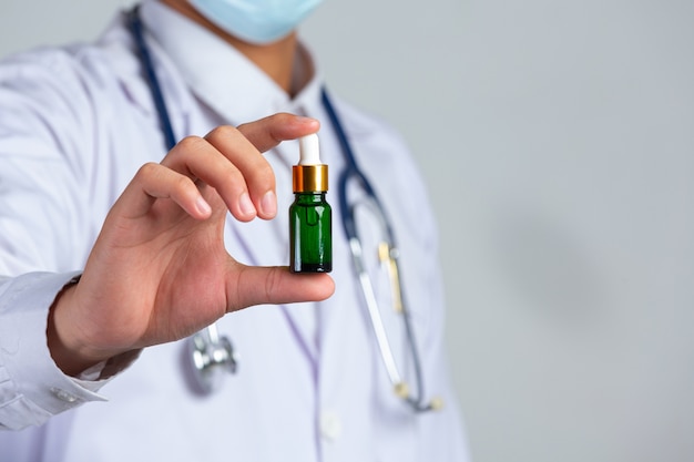 Cerrar imagen de médico sosteniendo una botella de aceite de cannabis en la pared blanca.