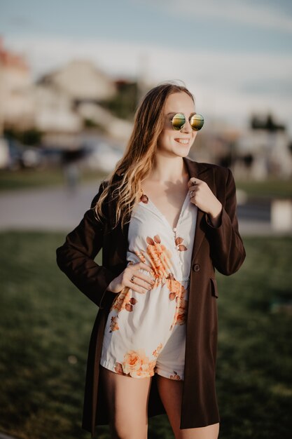 Cerrar imagen de mujer feliz en ropa de gafas de sol posando de lado al aire libre