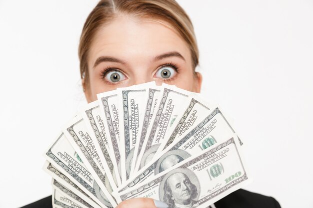Cerrar imagen de mujer de negocios rubia sorprendida escondiéndose detrás del dinero y sobre la pared blanca