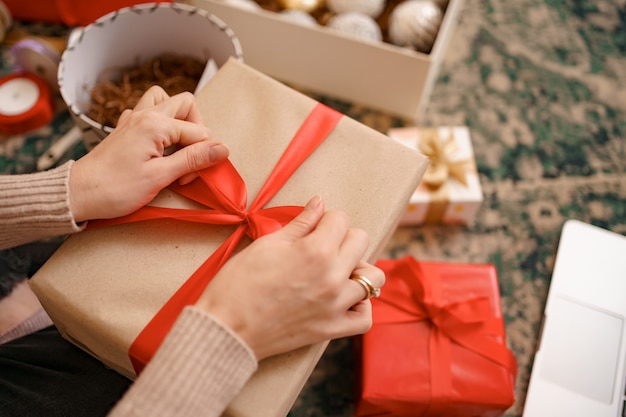 Cerrar las manos femeninas atando un lazo de cinta roja en una caja de regalo artesanal.
