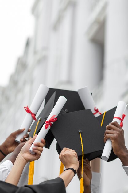 Cerrar manos sosteniendo diplomas y gorras