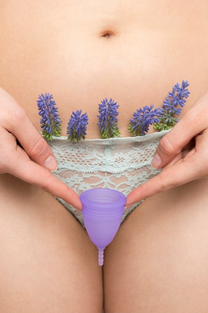 Cerrar mujer en bragas con flores de lavanda sosteniendo la copa menstrual