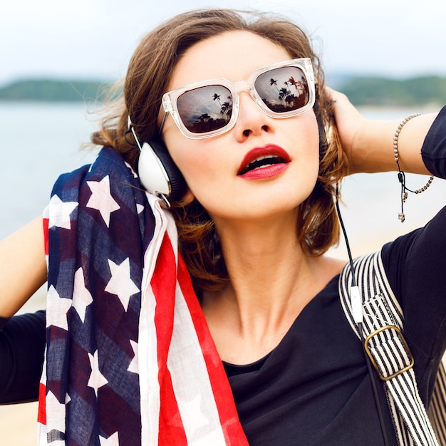 Cerrar mujer posando en la playa escuchando música en sus elegantes auriculares grandes