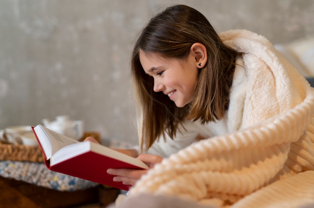 Cerrar niña leyendo en la cama