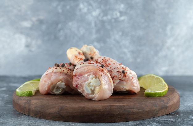 Foto gratuita cerrar las piernas de pollo marinado con rodajas de limón sobre tabla de madera.