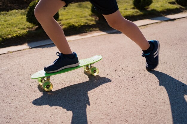 Cerrar las piernas en zapatillas azules montando en patineta verde en movimiento. Estilo de vida urbano activo de juventud, formación, hobby, actividad. Deporte activo al aire libre para niños. Niño en patineta.