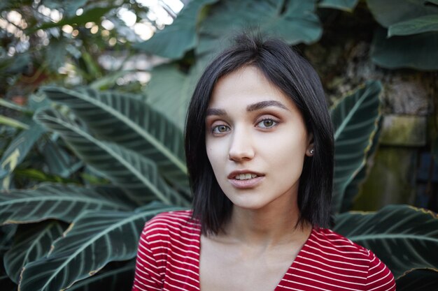 Cerrar un retrato al aire libre de una atractiva joven europea con un elegante corte de pelo bob que pasa tiempo en la naturaleza salvaje, con una expresión facial feliz y despreocupada, disfrutando de unas vacaciones en algún país tropical