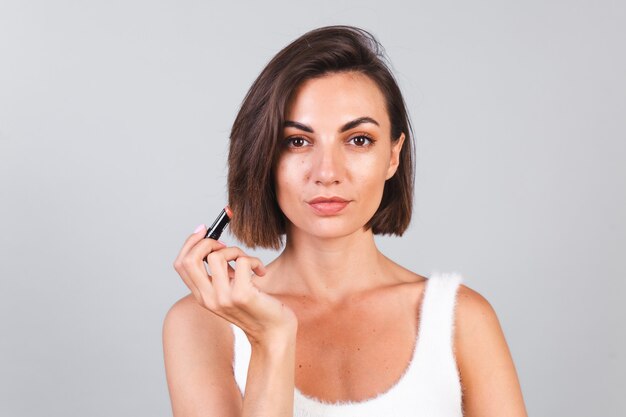 Cerrar retrato de belleza de mujer con maquillaje y lápiz labial marrón en pared gris