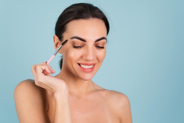 Cerrar el retrato de la belleza de una mujer con una piel perfecta y maquillaje natural, labios desnudos completos, sosteniendo un pincel para cejas