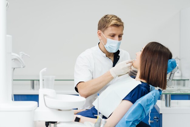 Cerrar retrato de hermosa joven sentada en el sillón dental mientras el estomatólogo manos en guantes estériles sosteniendo muestras de dientes