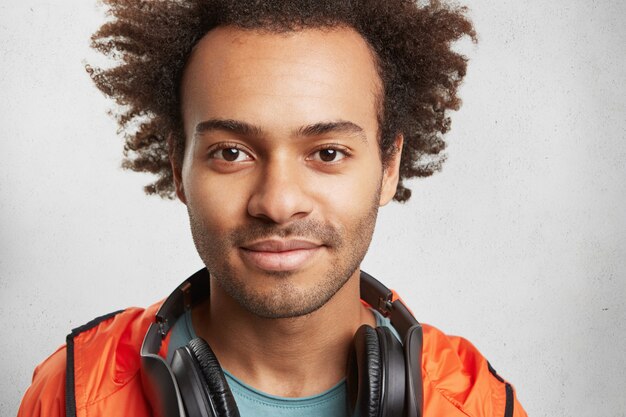 Cerrar retrato de hombre atractivo con peinado afro, rastrojo, viste anorak naranja