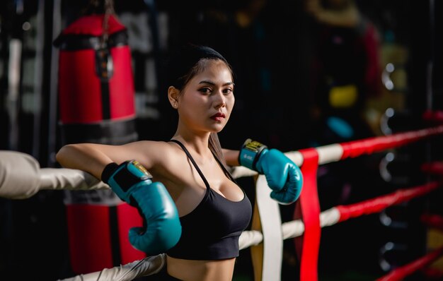 Cerrar retrato joven mujer bonita en guante de boxeo de pie sobre lienzo después de entrenar con cansado, entrenamiento en el gimnasio,
