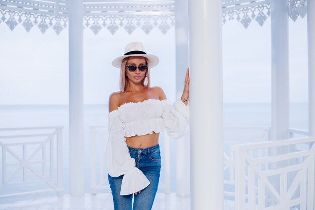 Cerrar retrato de moda al aire libre de mujer elegante en voluminoso top blanco de moda y sombrero de lujo clásico y gafas de sol de leopardo