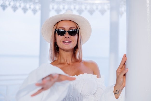 Foto gratuita cerrar retrato de moda al aire libre de mujer elegante en voluminoso top blanco de moda y sombrero de lujo clásico y gafas de sol de leopardo