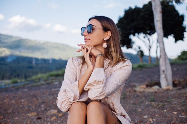 Cerrar retrato de mujer joven con gafas de sol y aretes al atardecer en el parque