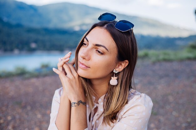 Cerrar retrato de mujer joven con gafas de sol y aretes al atardecer en el parque