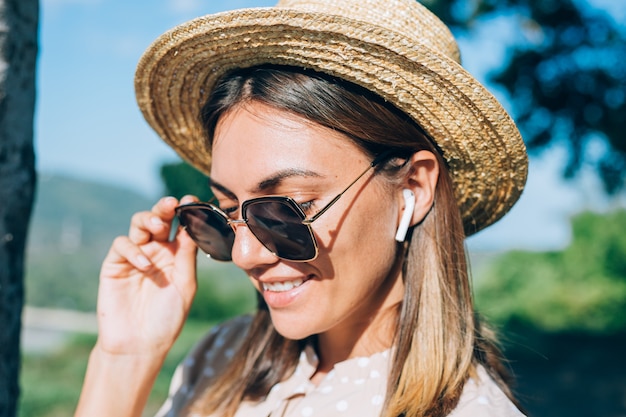 Foto gratuita cerrar retrato de mujer joven con gafas de sol y aretes al atardecer en el parque