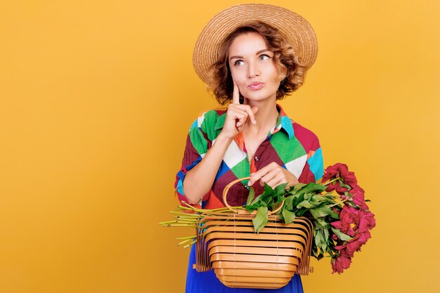 Foto gratuita cerrar retrato de mujer pensativa con peinado rizado con ramo de piones en las manos. fondo de pared amarilla.