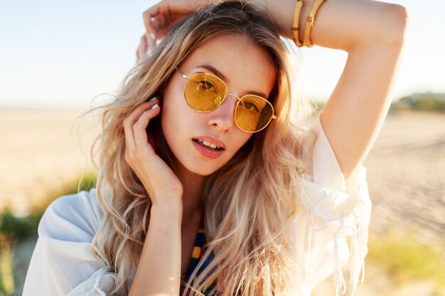 Cerrar retrato de niña rubia sonriente juguetona jugando con pelos, divirtiéndose y disfrutando del verano en la playa.